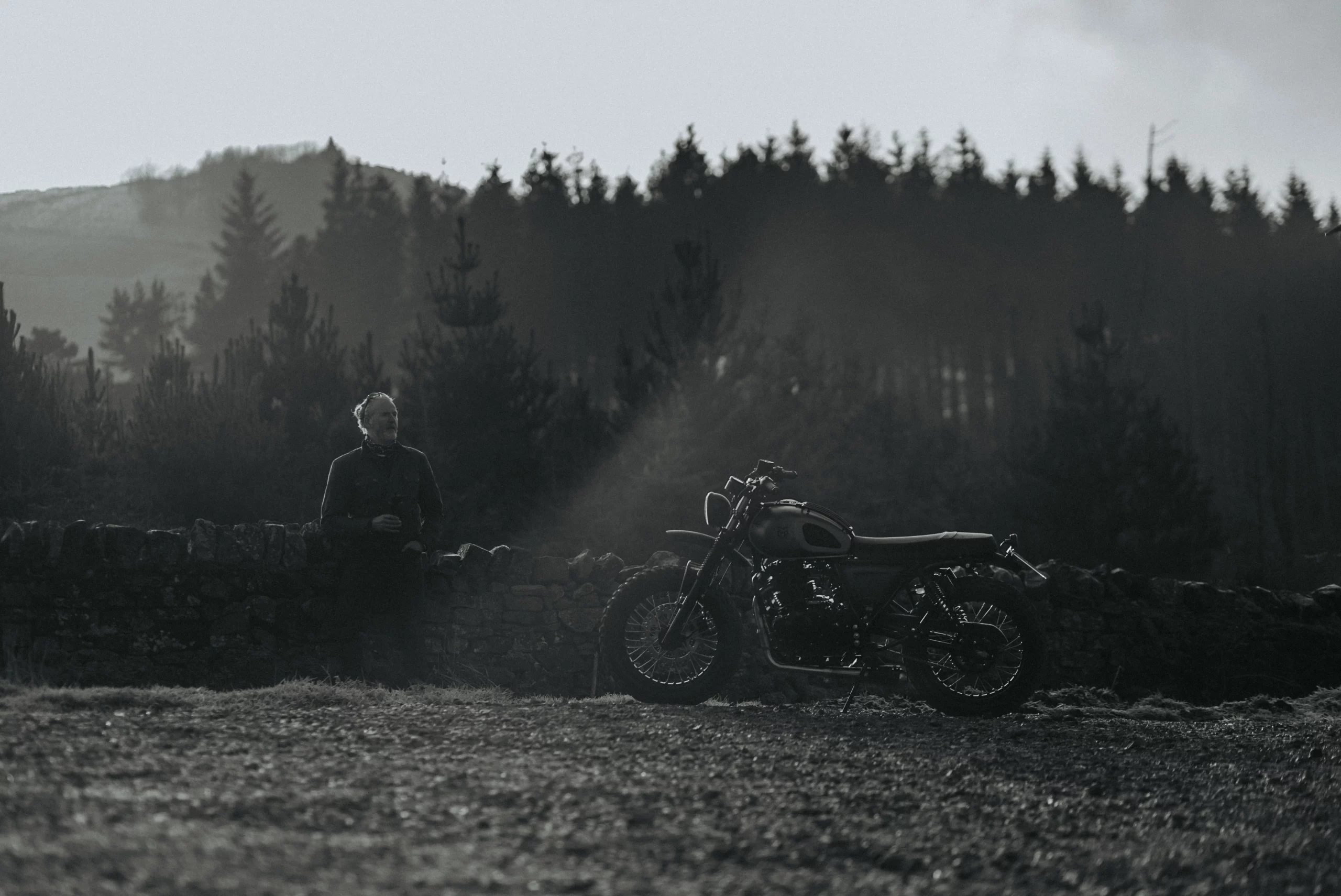 Man sitting on stone wall beside Mutt motorcycle after early morning ride