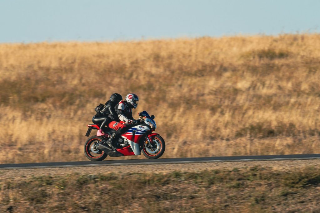 a-man-rwith-woman-passenger-riding-a-red-motorcycle-down-a-road-kJfugpeDwL0